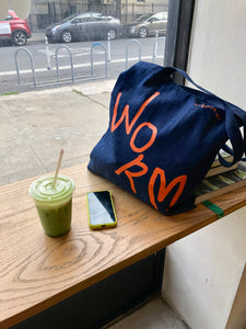 WORM DENIM TOTE BAG AT A CAFE NEXT TO ICED MATCHA LATTE AND PHONE